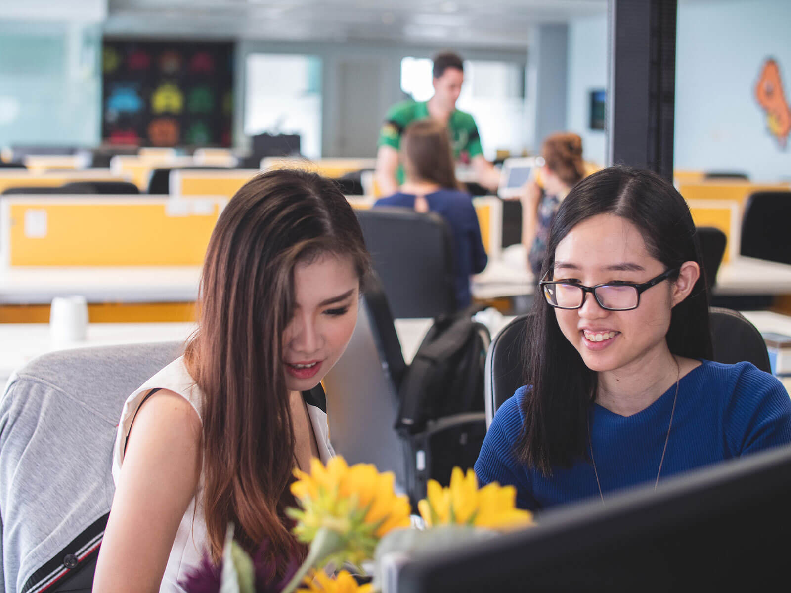 Two women sitting at a computer with sunflowers.